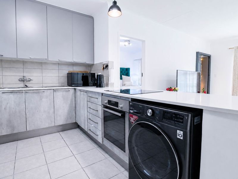 Modern kitchen featuring grey cabinetry, stone countertops, integrated oven and hob, and tiled flooring, seamlessly flowing into the adjacent living area.