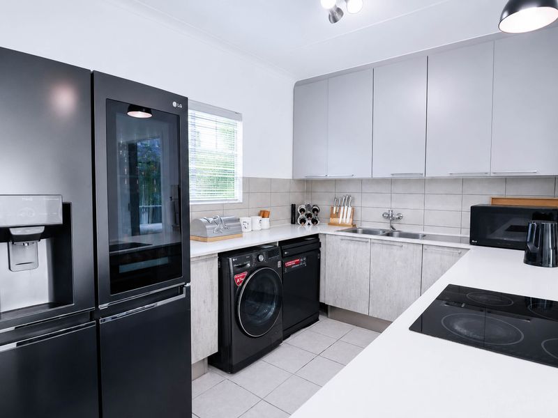 Modern kitchen featuring light grey cabinetry, white countertops, tiled splashback, integrated hob, and double sink with contemporary finishes.