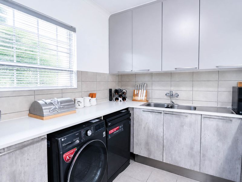 A functional scullery featuring modern grey cabinetry, a stainless steel sink, tiled backsplash, and dedicated space for laundry appliances.