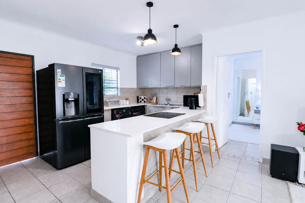 Modern kitchen featuring a central island with a built-in cooktop, sleek grey cabinetry, tiled backsplash, and contemporary pendant lighting.