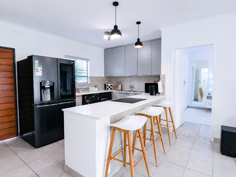 Modern kitchen featuring a central island with a built-in cooktop, sleek grey cabinetry, tiled backsplash, and contemporary pendant lighting.