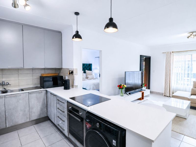Modern open-plan kitchen featuring sleek grey cabinetry, stone countertops, integrated appliances, and tiled flooring, seamlessly flowing into the adjacent living area.