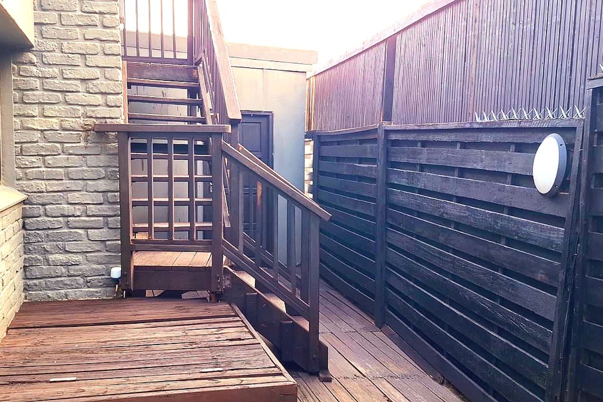 A side exterior passage featuring timber decking, a wooden staircase, and dark-stained timber privacy fencing with integrated wall lighting.