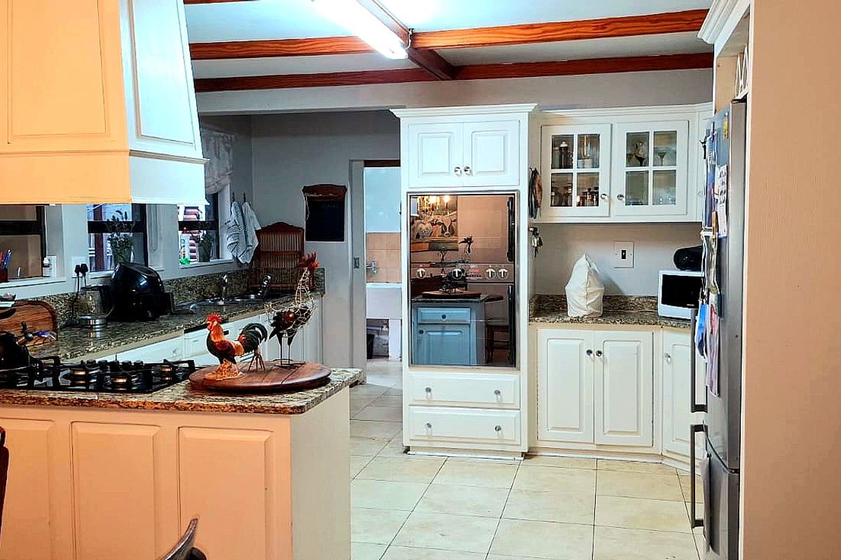 A functional kitchen featuring granite countertops, built-in oven, gas hob, and white cabinetry with exposed timber ceiling beams.