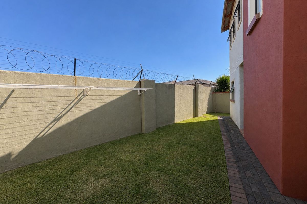 A private rear garden area featuring a paved walkway, lawn, and high boundary walls secured with razor wire.