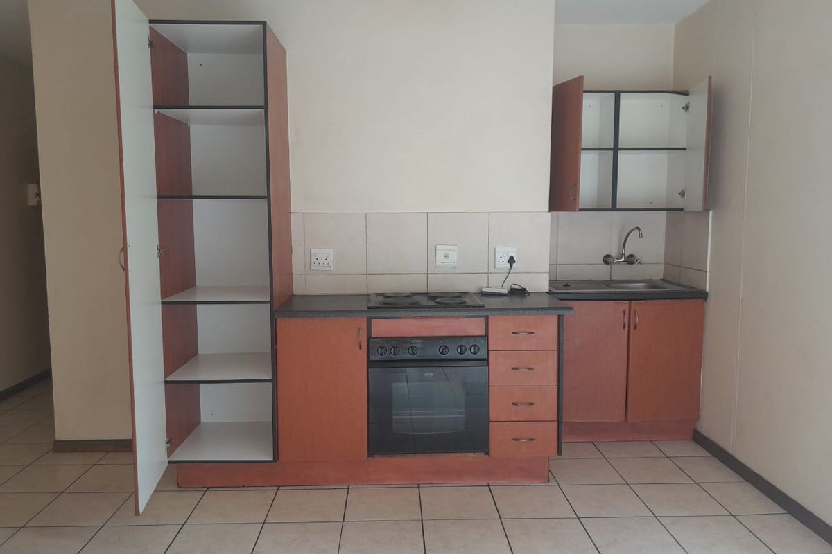A compact, dated kitchen featuring built-in cabinetry, an integrated oven and hob, and tiled flooring. The space is currently empty and ready for renovation.