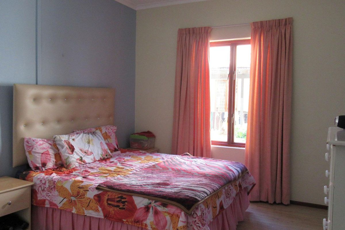 A functional bedroom featuring laminate flooring and a window with curtains, providing a comfortable and well-lit living space.