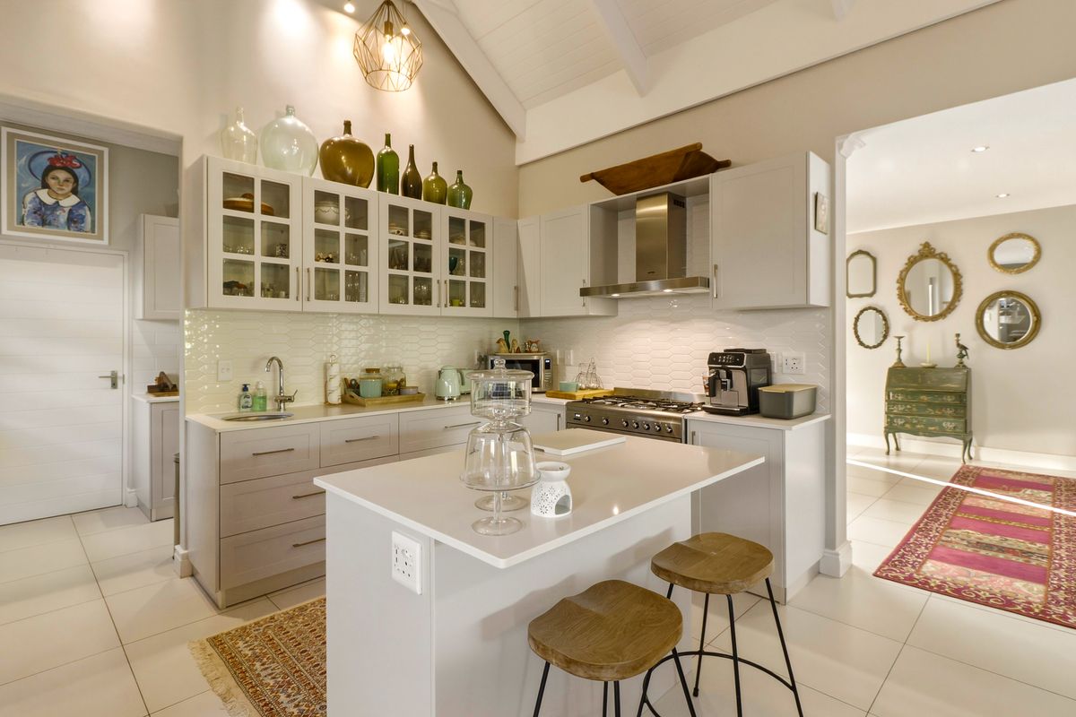 Modern kitchen featuring light grey cabinetry, stone countertops, gas cooktop, extractor fan, and a central island, set under a high vaulted ceiling.
