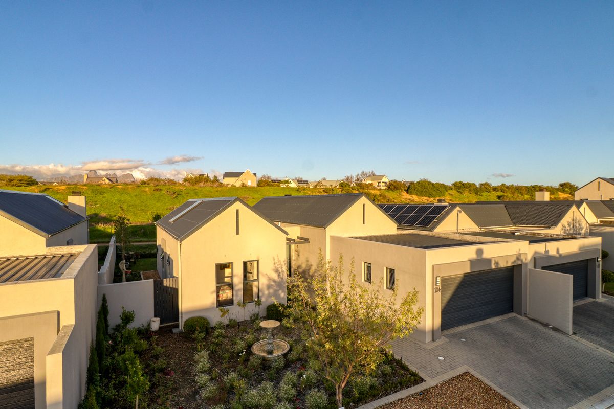 Aerial view of a modern residential property featuring a paved driveway, double garage, solar panels, and a well-maintained landscaped front garden.
