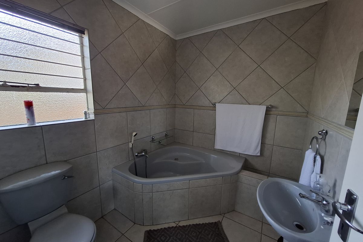 A functional bathroom featuring a corner bathtub, pedestal basin, toilet, and neutral wall and floor tiling.