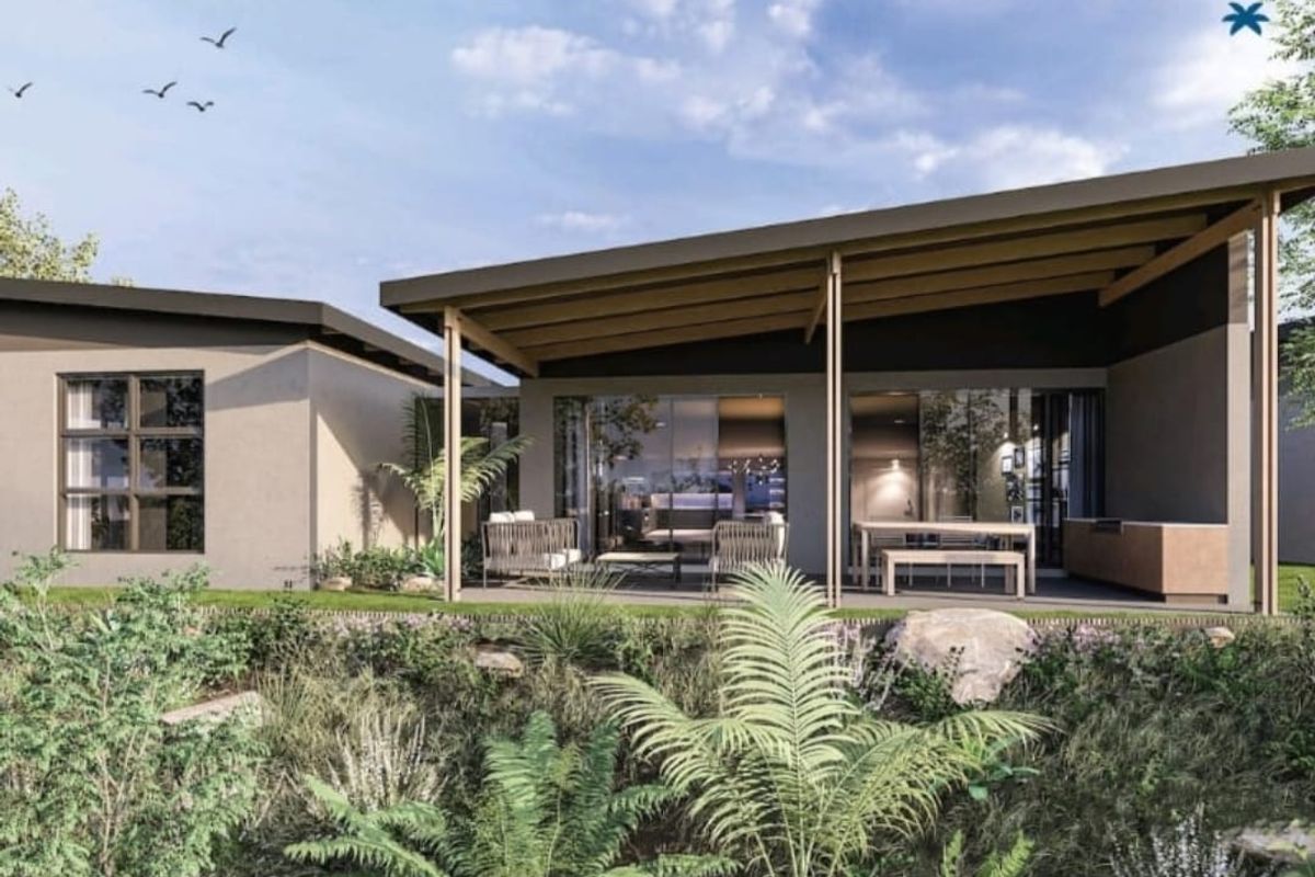 A modern rear exterior view of a cluster home featuring a covered patio, large sliding glass doors, and a landscaped garden area.