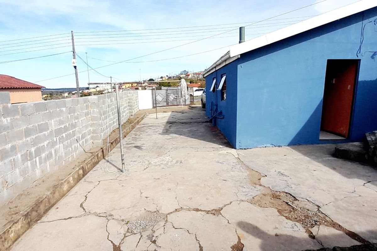 Rear exterior area featuring a concrete paved yard, cinder block boundary wall, and blue painted exterior wall.