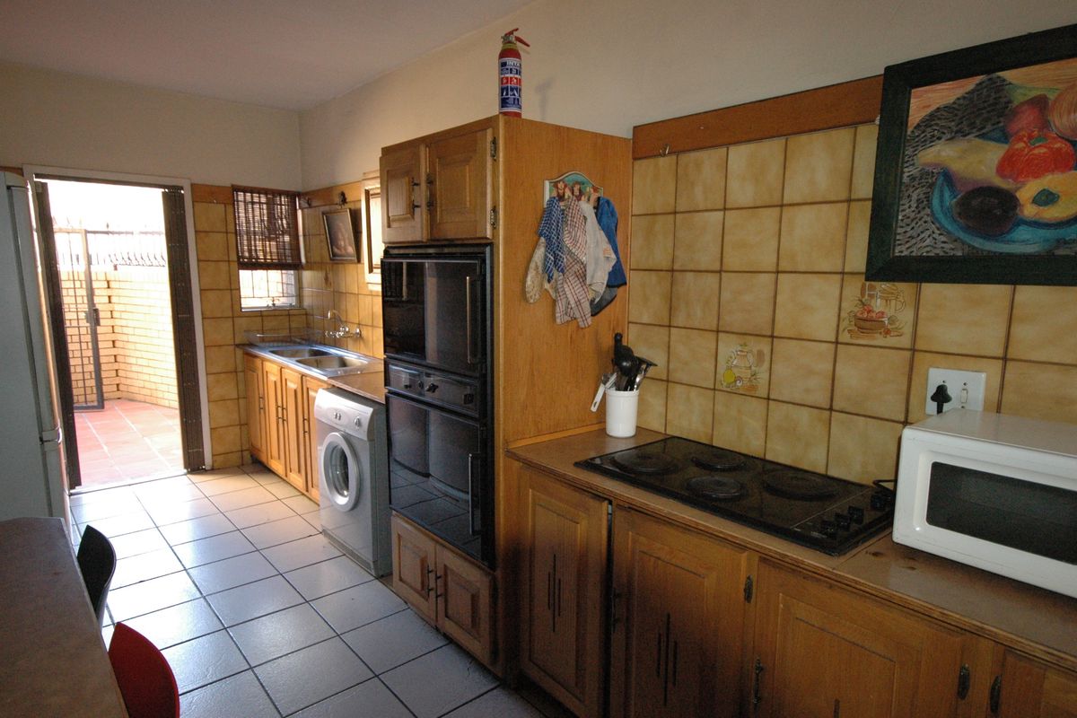 A functional kitchen featuring traditional wooden cabinetry, tiled backsplash, built-in oven, electric hob, and direct access to an outdoor patio area.