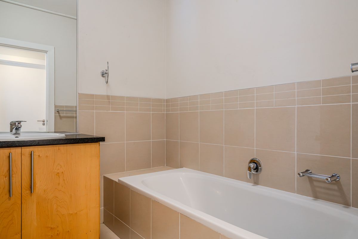 A clean, functional bathroom featuring a built-in vanity with a dark countertop, a bathtub with wall-mounted fixtures, and neutral wall tiling.
