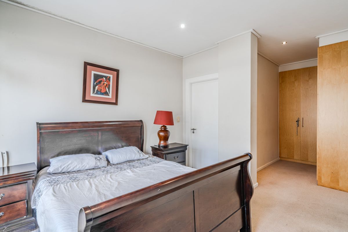 A well-lit bedroom featuring built-in wooden cupboards, neutral wall finishes, and carpeted flooring, providing a functional and comfortable living space.