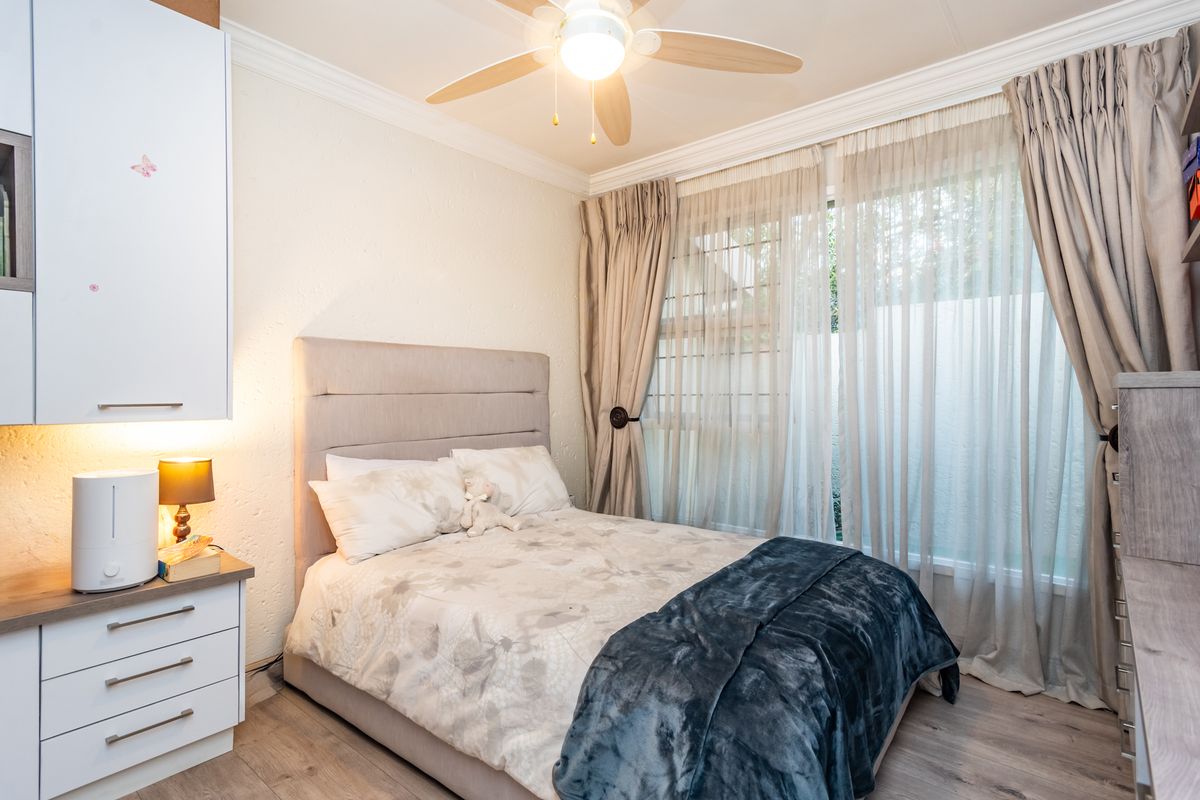 A well-maintained bedroom featuring laminate flooring, built-in cabinetry, a ceiling fan, and large windows with security bars.