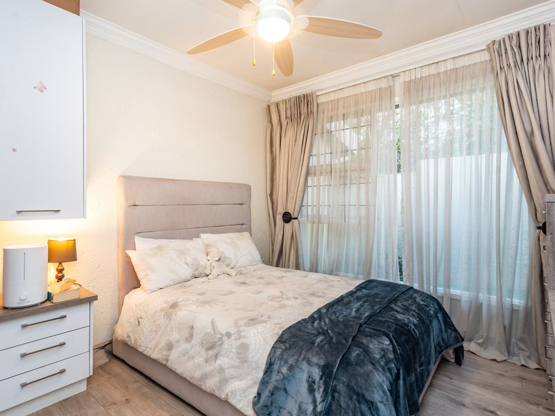 A well-maintained bedroom featuring laminate flooring, built-in cabinetry, a ceiling fan, and large windows with security bars.