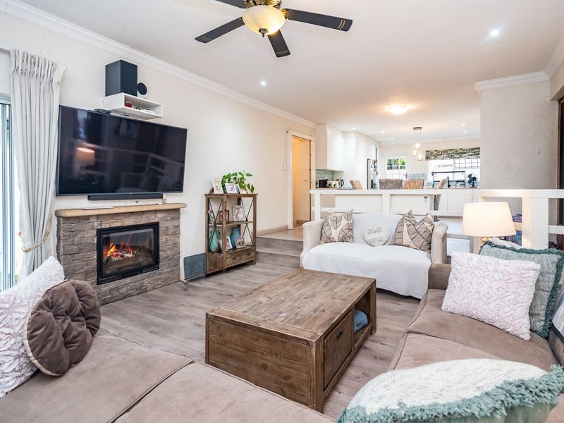 Spacious open-plan living area featuring a stone-clad fireplace, laminate flooring, and a seamless flow into the modern kitchen with a central island.