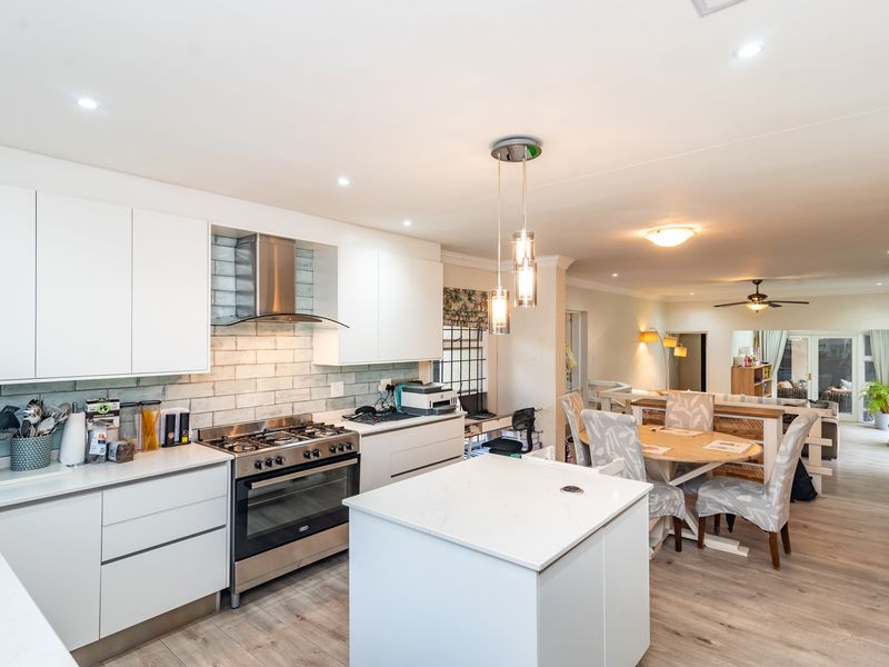 Modern open-plan kitchen featuring white cabinetry, a central island, gas stove with extractor, and subway tile backsplash, flowing into the dining and living areas.