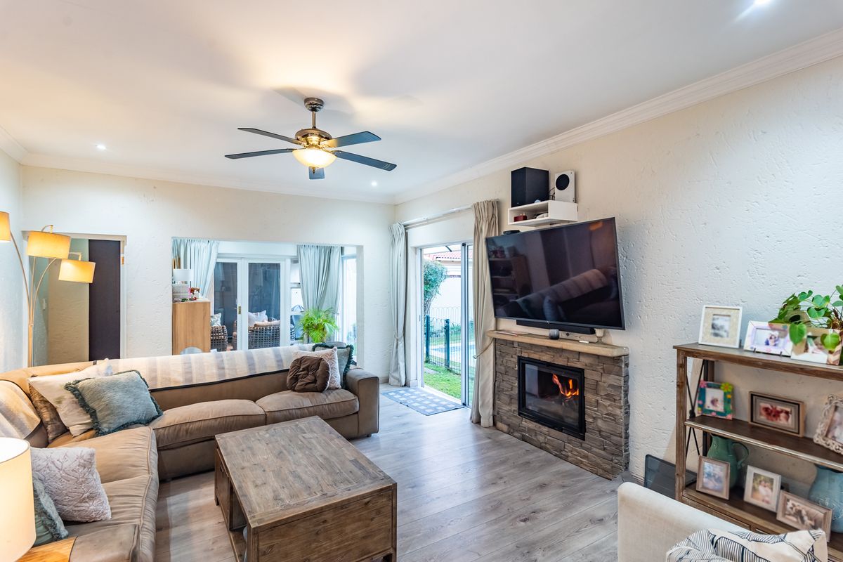 Spacious living room featuring a stone-clad fireplace, laminate flooring, ceiling fan, and large sliding glass doors providing access to the outdoor area.