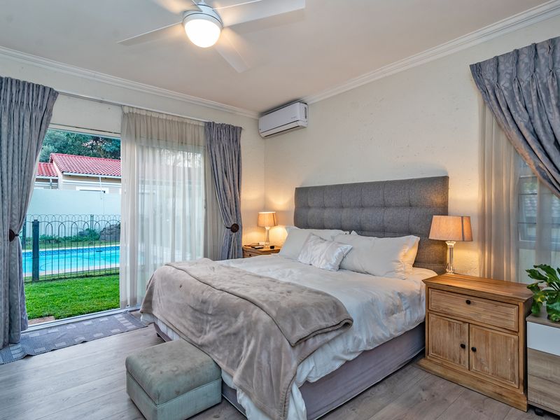 Spacious bedroom featuring laminate flooring, a ceiling fan, air conditioning, and direct access to a private garden and pool area through sliding glass doors.