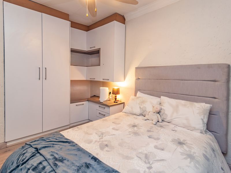 A well-maintained bedroom featuring built-in cupboards with integrated desk space, laminate flooring, and a ceiling fan.