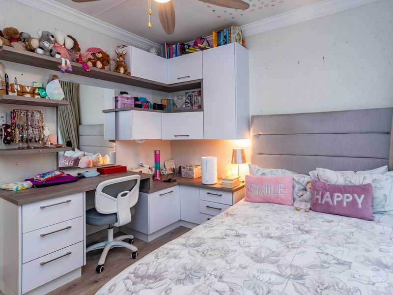 A well-maintained bedroom featuring custom built-in cabinetry, a integrated desk workspace, laminate flooring, and a ceiling fan.