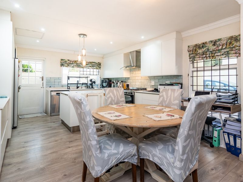 Open-plan kitchen and dining area featuring modern white cabinetry, a central island, subway tile backsplash, and durable laminate flooring with direct exterior access.