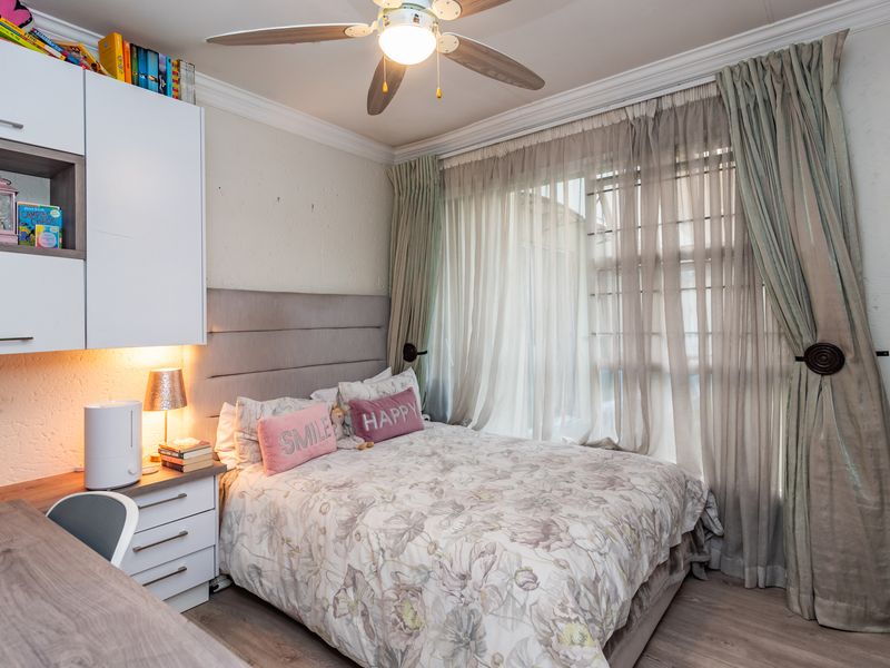 A well-maintained bedroom featuring built-in cabinetry, a desk, laminate flooring, and a ceiling fan, with natural light filtered through window curtains.