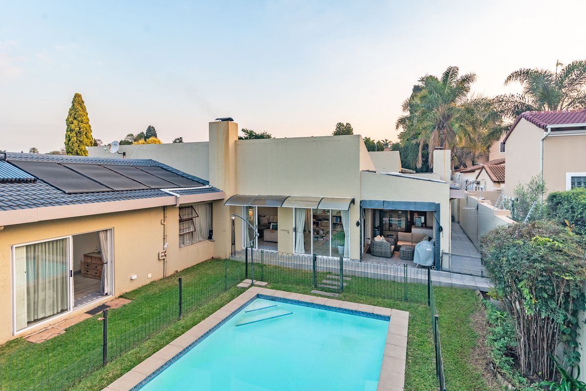 Rear view of the property featuring a swimming pool with solar heating panels, a paved patio area, and sliding glass door access to the home.