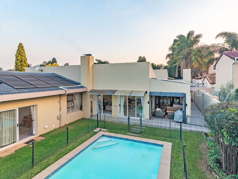 Rear view of the property featuring a swimming pool with solar heating panels, a paved patio area, and sliding glass door access to the home.