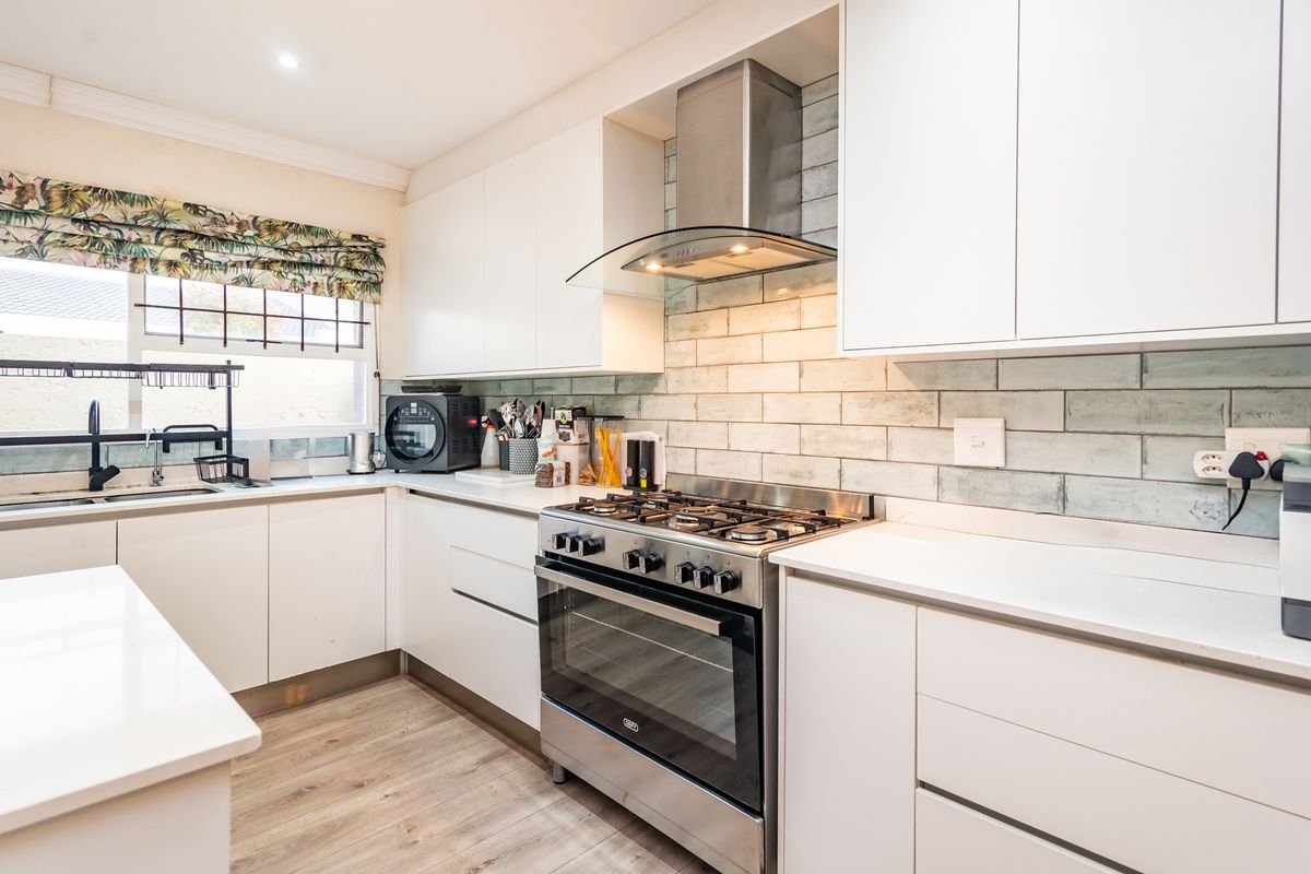 Modern kitchen featuring white cabinetry, quartz countertops, a gas stove with extractor fan, and a stylish subway tile backsplash.