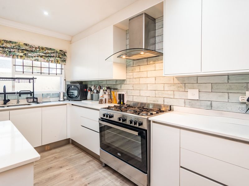 Modern kitchen featuring white cabinetry, quartz countertops, a gas stove with extractor fan, and a stylish subway tile backsplash.