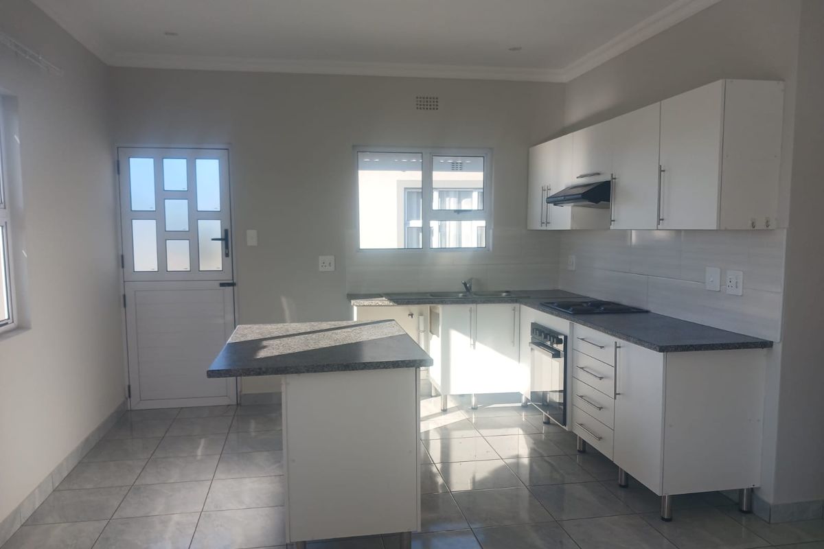 A clean, modern kitchen featuring white cabinetry, granite countertops, built-in oven and hob, and tiled flooring with direct access to the exterior.