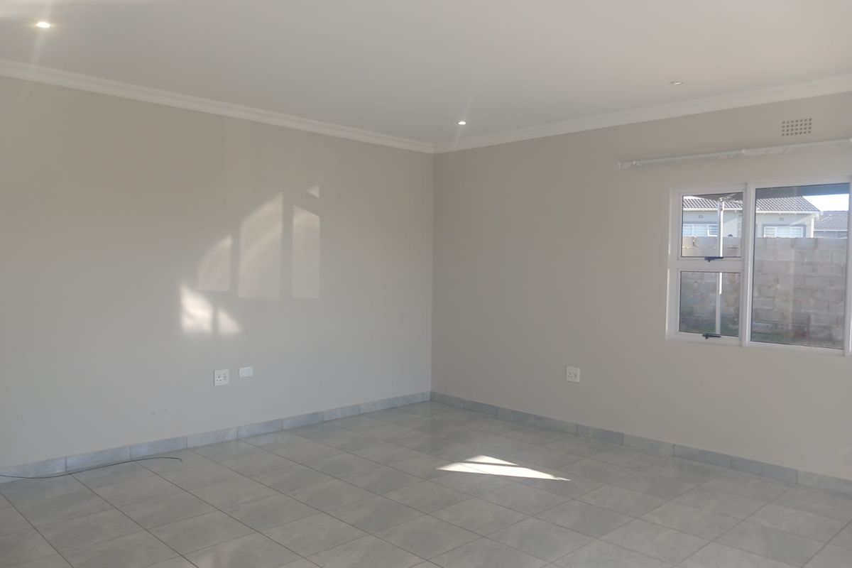 A bright, empty living room featuring neutral walls, tiled flooring, and recessed downlights, offering a clean and versatile space ready for furnishing.