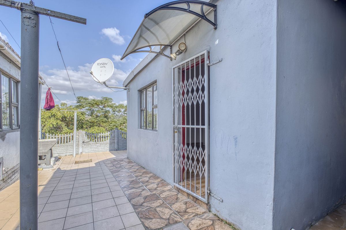 Rear exterior view of the property featuring a tiled patio area, security gate, and wall-mounted satellite dish.