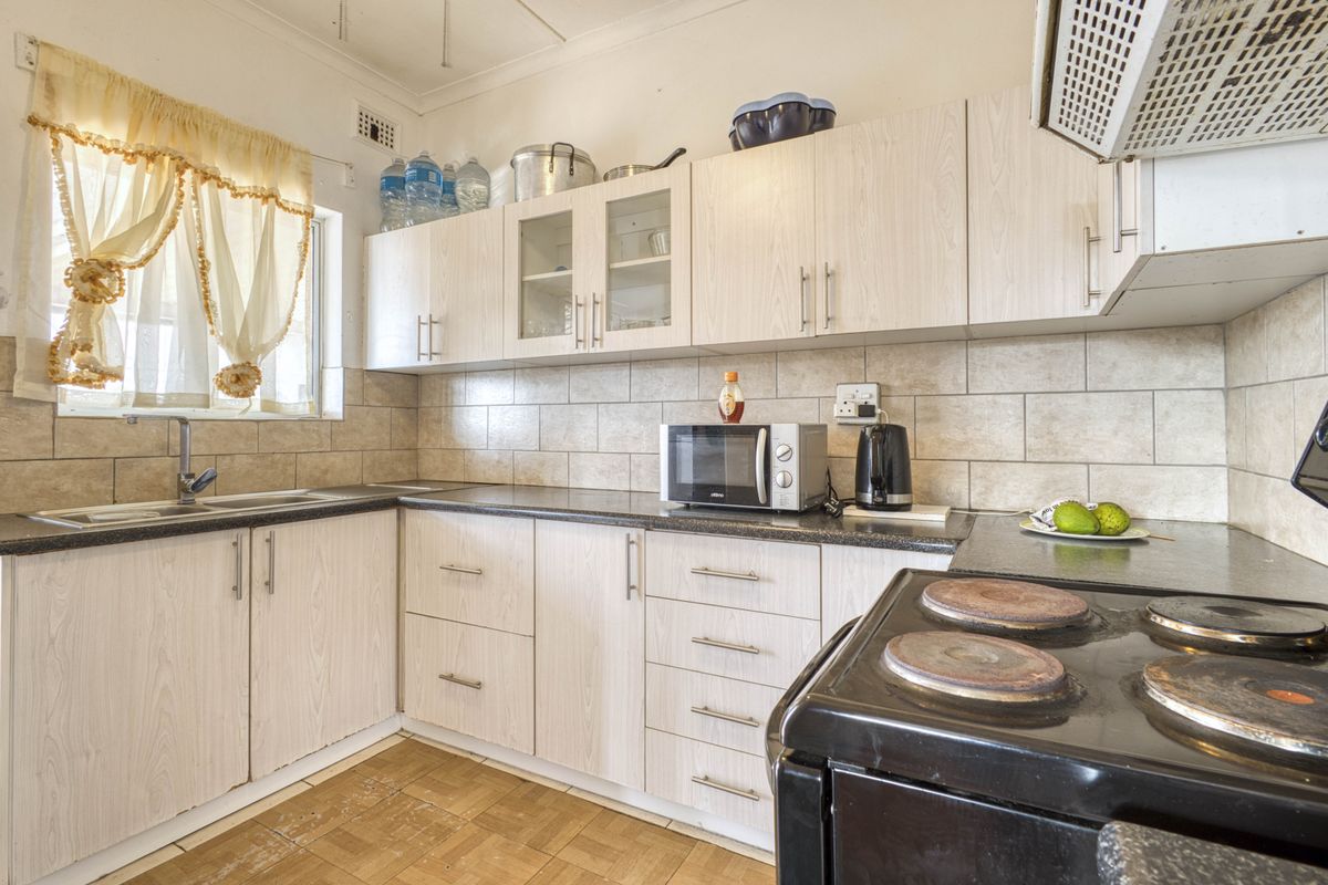 Functional kitchen featuring light wood-look cabinetry, tiled backsplash, laminate countertops, and a built-in extractor fan.