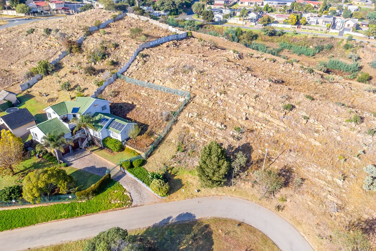 Aerial view of a residential vacant land plot featuring rocky terrain, perimeter fencing, and adjacent established housing with solar infrastructure.