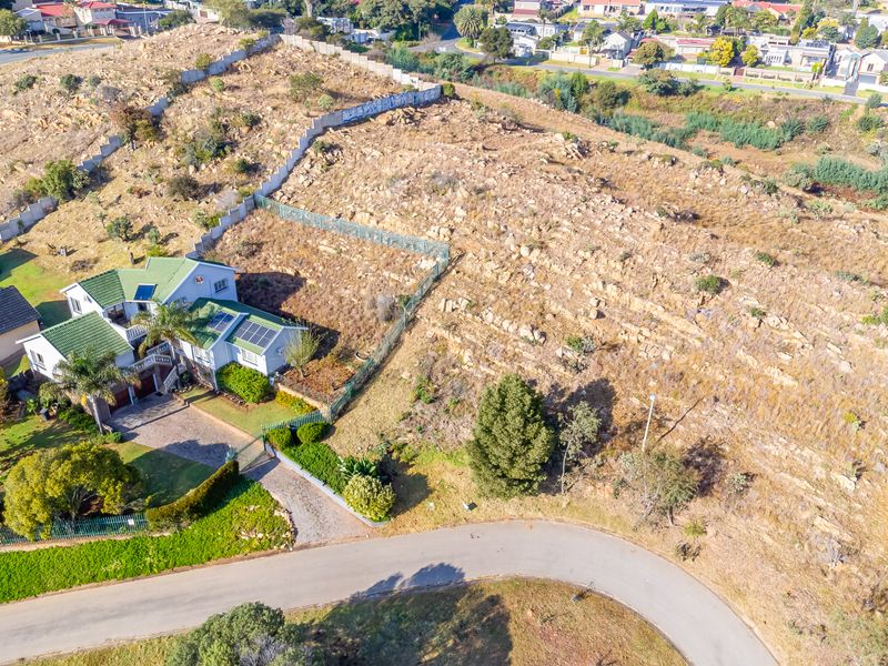 Aerial view of a residential vacant land plot featuring rocky terrain, perimeter fencing, and adjacent established housing with solar infrastructure.