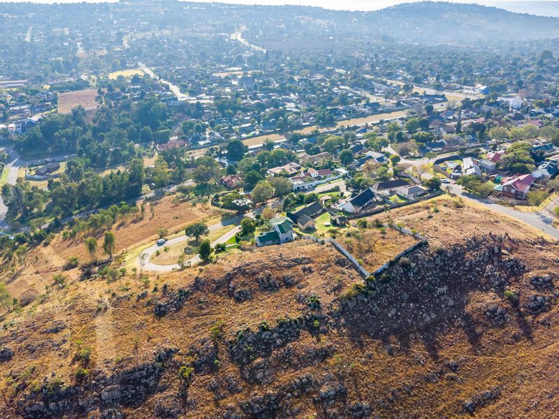 Aerial view of a vacant residential plot featuring rocky terrain and boundary fencing, situated in an established suburban neighborhood.