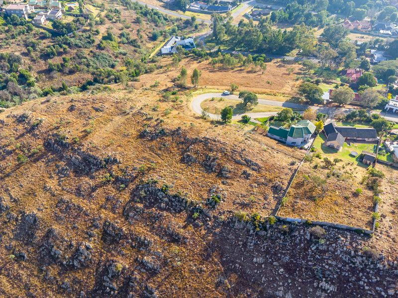 An aerial view of a vacant residential plot featuring rocky terrain, natural vegetation, and established boundary fencing in a suburban setting.