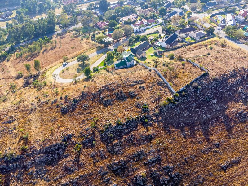 Aerial view of a vacant residential plot featuring natural rocky terrain and partial boundary walling in an established suburban area.
