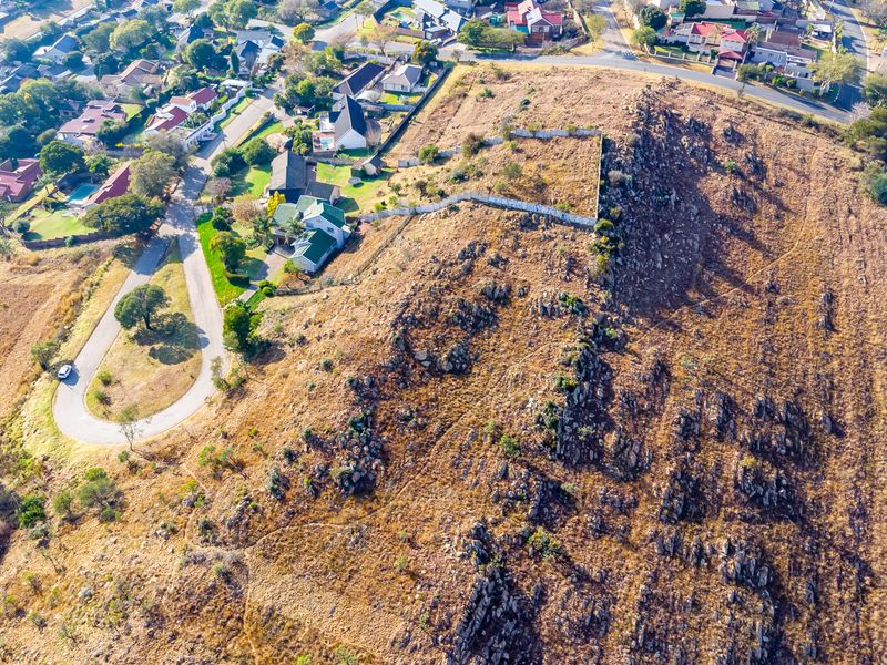 An aerial view of a vacant residential plot featuring rocky terrain and perimeter fencing, situated within an established suburban neighborhood.
