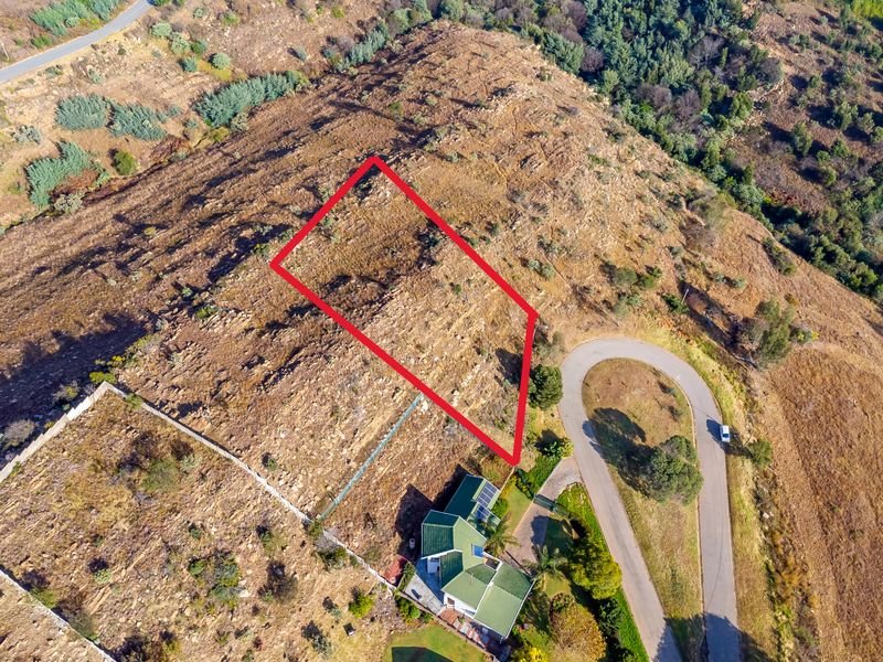 An aerial view of a vacant residential plot featuring sloped, rocky terrain with clear boundary markings, situated in a hillside neighborhood.