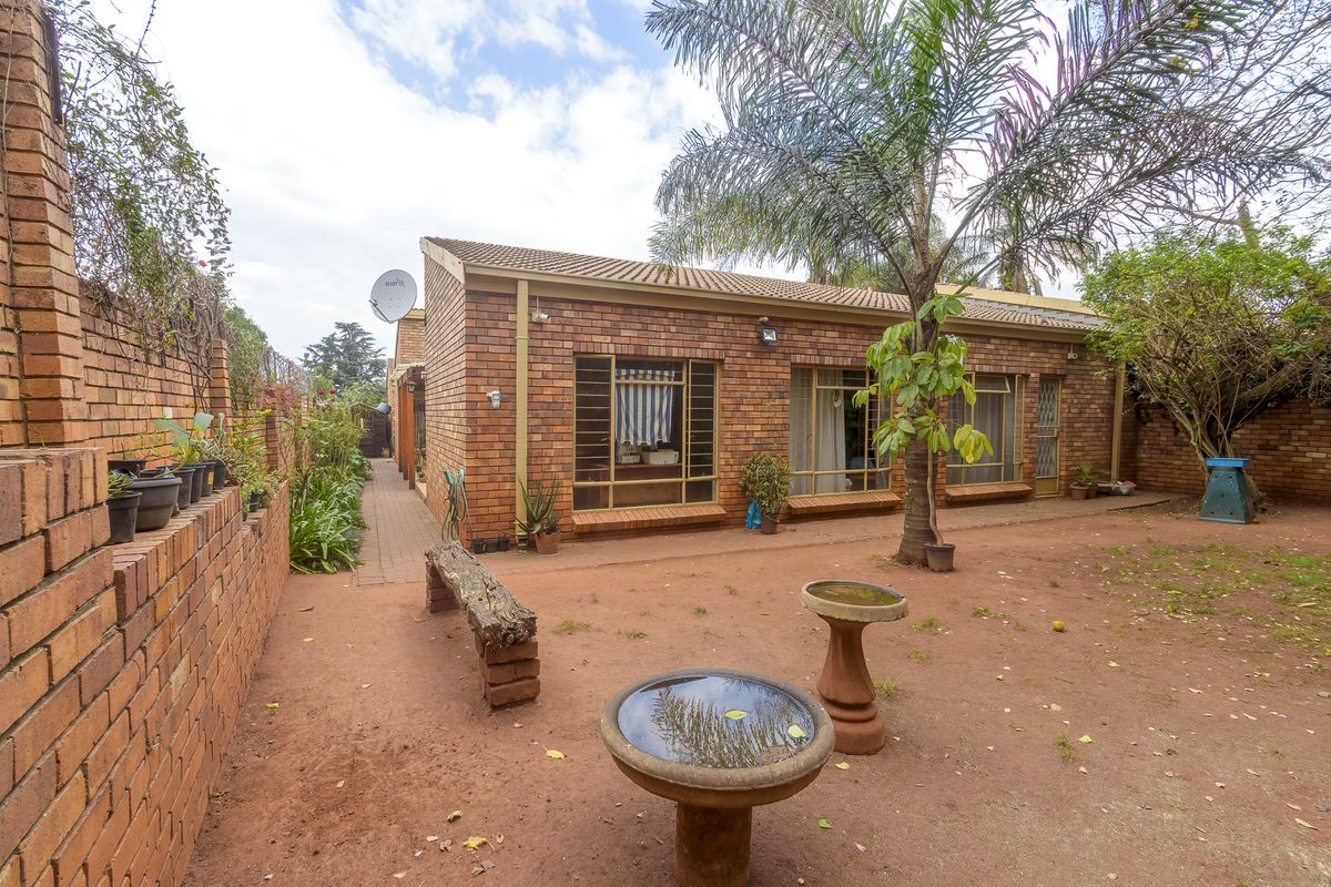 Rear exterior view of a face brick townhouse featuring a paved walkway, large windows, and a private garden area.