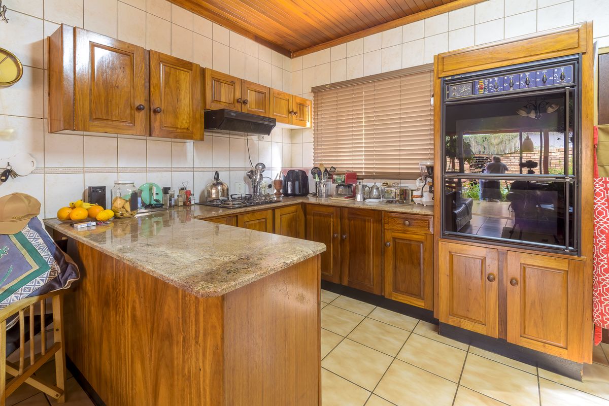 A functional kitchen featuring wooden cabinetry, granite countertops, a built-in oven, gas hob, and tiled finishes throughout.