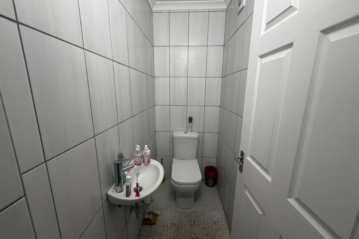 A compact guest bathroom featuring floor-to-ceiling wall tiles, a wall-mounted basin, and a standard toilet.