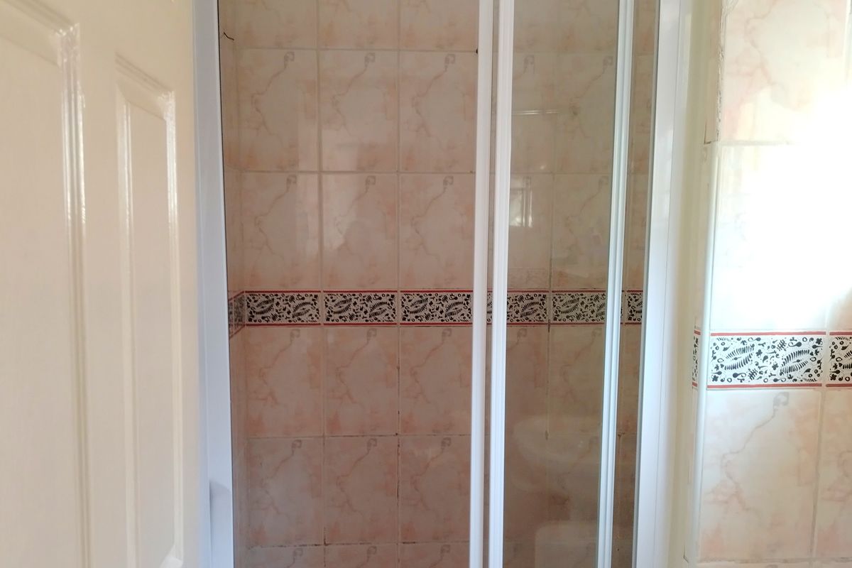 A bathroom shower enclosure featuring dated wall and floor tiling with a white frame sliding door.