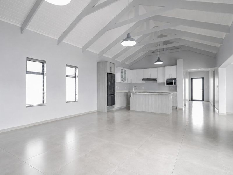 Spacious open-plan living and kitchen area featuring high vaulted ceilings with exposed rafters, modern cabinetry, a central island, and neutral tiled flooring throughout.