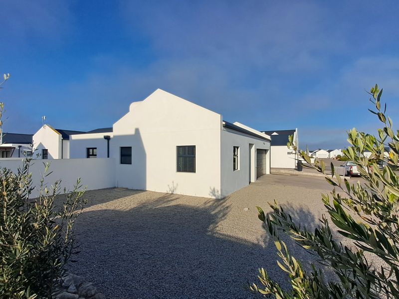 A modern white-walled house exterior featuring a gravel driveway, secure boundary wall, and integrated garage, set against a clear blue sky.